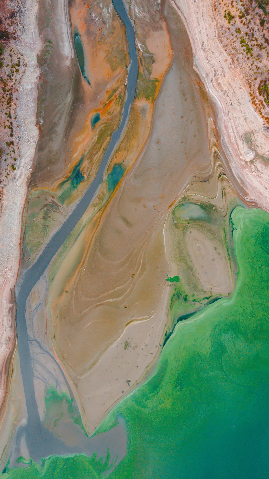 Aerial view of a river channel crossing mudflats into green water